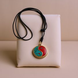 Handmade in Nepal by skilled artisans, this pendant necklace embodies the harmony of Yin and Yang, inviting inner peace through its brass, Turquoise, and Coral elements.