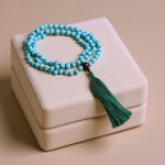 This handmade Blue Turquoise prayer stone mala from Nepal, with its gentle tassel, is a sacred tool for meditation and spiritual connection, enhancing communication and balancing the heart chakra.