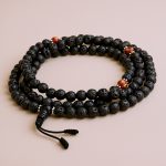 Lava Stone Yoga Mala with Carnelian Spacer, handmade in Nepal by skilled artisans, supports meditation by promoting emotional balance and fostering vitality on your spiritual journey.