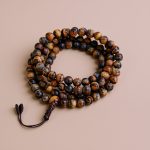 This handmade Tiger Eye Stone Japa Mala from Nepal connects the wearer to the universe, enhancing meditation and focus while embodying the blessings of strength and adventure on one's spiritual path.