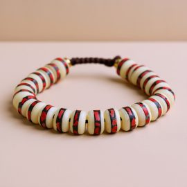 Handmade in Nepal by skilled artisans, this Inlaid Yak Bone Wrist Mala with red coral stones embodies the essence of Vajrayana Buddhism, supporting meditation and reflection on life's impermanence.