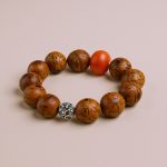 Antique Light Brown Phoenix Eye Bodhi Seed Wrist Mala, handcrafted in Nepal, features a coral bead and Tibetan mantra bead, symbolizing wisdom, peace, and spiritual protection on your journey.