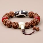 The Tibetan Dzi 5 Faces Rudraksha Seed Wrist Mala, handmade in Nepal by skilled artisans, embodies spiritual protection and invites the blessings of Lord Shiva into your practice.