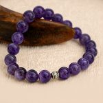 This Healing Amethyst Stone Wrist Mala, handmade in Nepal by skilled artisans, features calming amethyst and white metal beads, serving as a powerful tool for enhancing healing and promoting inner peace.