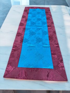 This handmade Tibetan table runner, crafted by skilled artisans in Nepal, features the sacred endless knot, symbolizing life's interconnectedness, and enriches your meditation space with its vibrant colors.