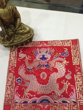 This handmade Tibetan silk brocade placemat, crafted by skilled artisans in Nepal, features a dragon symbolizing strength, enriching your sacred space during prayer and meditation.