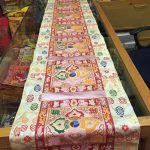 This handmade Tibetan table runner, crafted from silk brocade in Nepal, features a serene white base with baby pink accents and a central double dorje symbol, enhancing your meditation space.