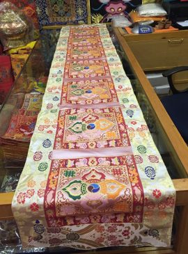 This handmade Tibetan table runner, crafted from silk brocade in Nepal, features a serene white base with baby pink accents and a central double dorje symbol, enhancing your meditation space.