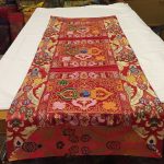 This handmade Tibetan table runner from Nepal, adorned with a double dorje and floral motifs, enriches your meditation space with vibrant colors and fosters a serene atmosphere.