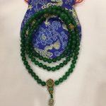 This handmade mala from Nepal features 108 jade beads, promoting serenity and emotional balance, with a guru bead showcasing a tranquil Buddha face, all beautifully strung on a green cord.