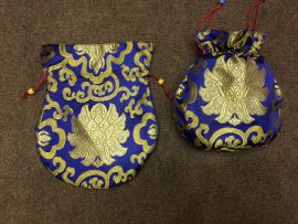 This handmade blue silk brocade mala bag, adorned with a lotus design, is crafted by skilled artisans in Nepal, providing a sacred space for your mala and versatile storage for daily essentials.