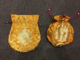 This handmade orange silk brocade mala bag, adorned with a lotus design, is crafted by skilled artisans in Nepal, embodying the essence of Tibetan Buddhism and spiritual practice.