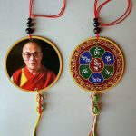 This handmade Dalai Lama car hanging, crafted in Nepal by skilled artisans, features the serene image of the Dalai Lama and the sacred mantra "Om Mani Padme Hum," inviting blessings and positive energy.