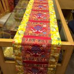 This handmade Tibetan table runner, crafted in Nepal by skilled artisans, features the endless knot, symbolizing life's interconnectedness and bringing harmony to your meditation space or home.