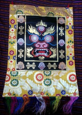 This handmade silk brocade wall hanging, crafted in Nepal, features the Mahakala design, embodying powerful protection and inviting spiritual blessings into your sacred space.