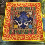 This handmade Tibetan altar cloth, crafted by skilled artisans in Nepal, features the blue endless knot and a lotus border, symbolizing life's interconnectedness and inviting spiritual harmony.